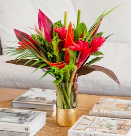 Vibrant tropical flower arrangement featuring red blooms and lush green foliage in a stylish vase.