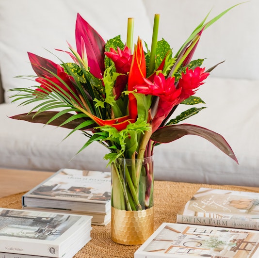 Vibrant tropical flower arrangement featuring red blooms and lush green foliage in a stylish vase.