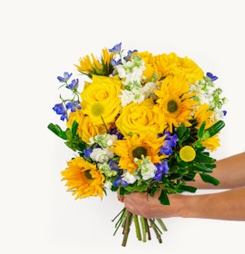 Vibrant bouquet of yellow roses, sunflowers, and blue delphiniums, perfect for celebrations.