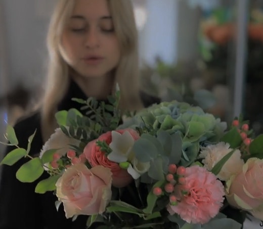 A beautiful floral arrangement featuring pink roses, greenery, and delicate blooms held by a woman.