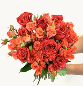 Vibrant bouquet of red and orange roses with lush green leaves, perfect for celebrations.