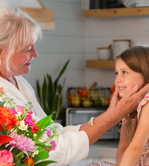 A joyful moment between a grandmother and granddaughter, surrounded by a vibrant floral bouquet.