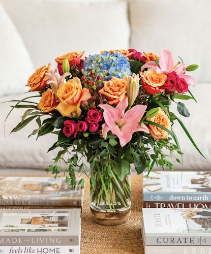 Vibrant mixed flower arrangement featuring roses, lilies, and hydrangeas in a glass vase.