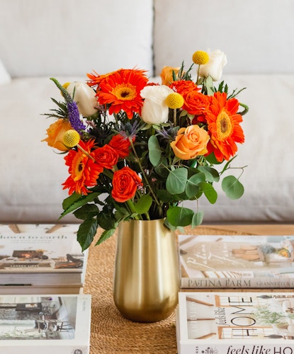 Vibrant mixed flower bouquet featuring orange gerberas, roses, and white blooms in a stylish vase.