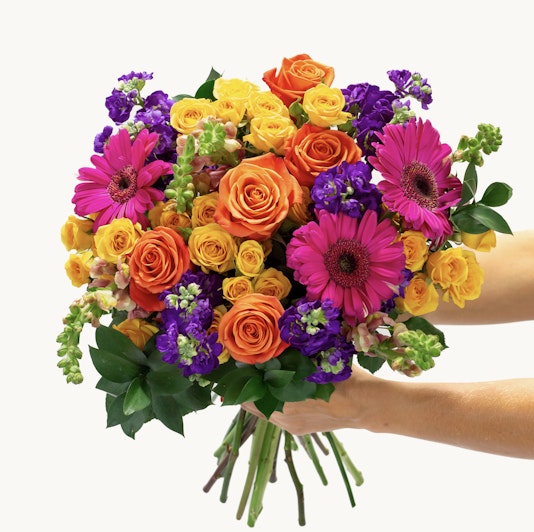 Bright and cheerful bouquet featuring orange roses, pink gerbera daisies, and vibrant green foliage.
