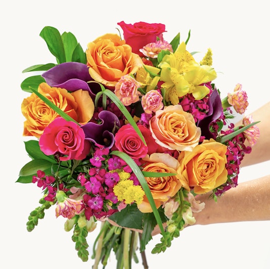 Vibrant bouquet featuring orange roses, purple blooms, and lush greenery, ideal for celebrations.