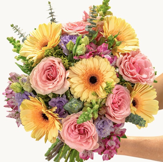 Bright and cheerful bouquet of yellow gerberas, pink roses, and lush greenery.