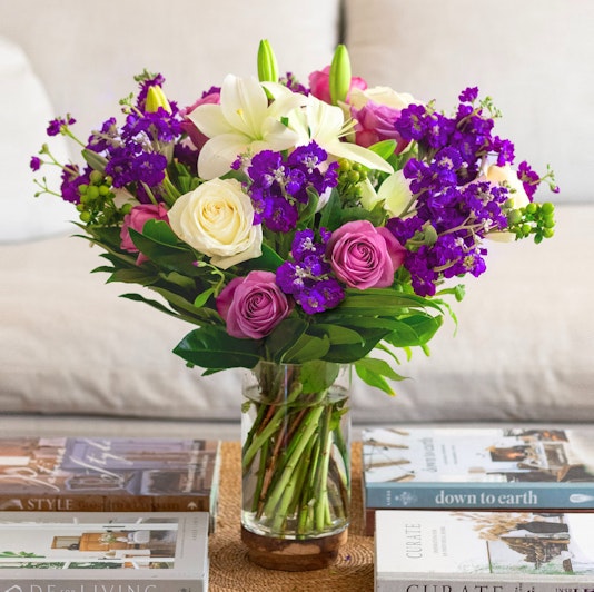 Vibrant mixed flower bouquet featuring purple, pink, and white blooms in a glass vase.